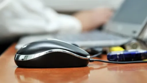 Computermaus mit arbeitender Person im Hintergrund