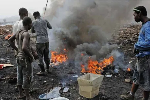 Junge Arbeiter in Agbogbloshie stehen beim Kabelabbrennen  zur Gewinnung von Kupfer im giftigen Rauch